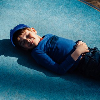 Junge liegt lächelnd auf blauer Drehscheibe am Spielplatz