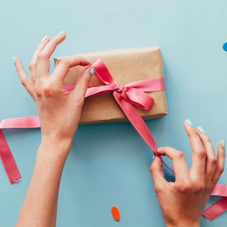 Frau bindet pinke Schleife um ein in Packpapier gewickeltes Geschenk