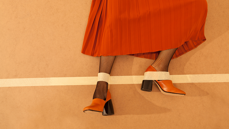 Füße in orange-schwarzen Highheels, die mit Kreppband am Boden festgeklebt wurden
