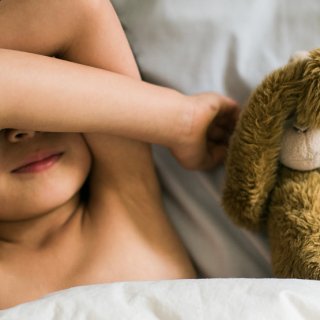Kind mit Ohrenschmerzen liegt im Bett mit Stofftier