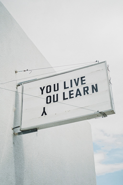 Schild an Hauswand mit Spruch "You live, you learn"