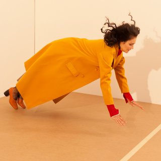 Frau in orangem Mantel lässt sich nach vorne fallen
