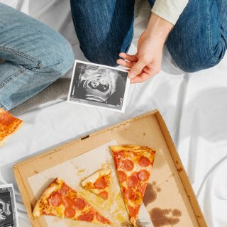 Zwei Menschen betrachten Ultraschallbilder einer Schwangeren beim Pizzaessen