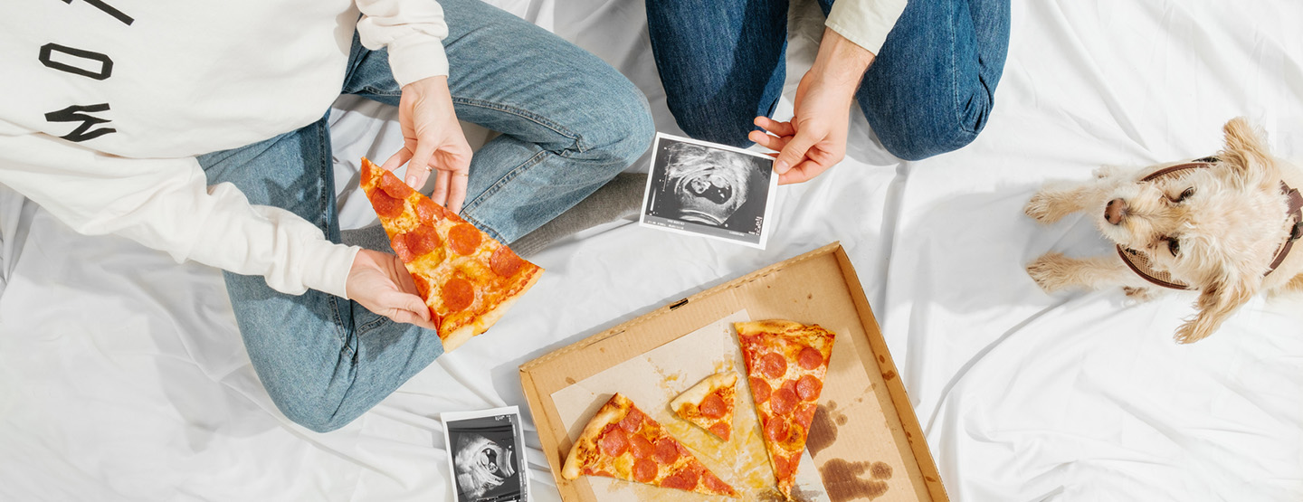 Zwei Menschen betrachten Ultraschallbilder einer Schwangeren beim Pizzaessen