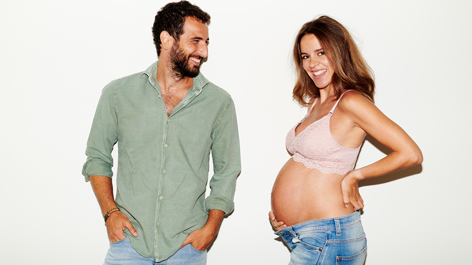 Schwangere mit BH und nacktem Bauch neben ihrem Partner in grünem Hemd