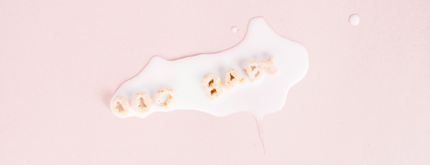 Das Wort Baby mit Cerealien gelegt in weißer Milch auf rosa Hintergrund