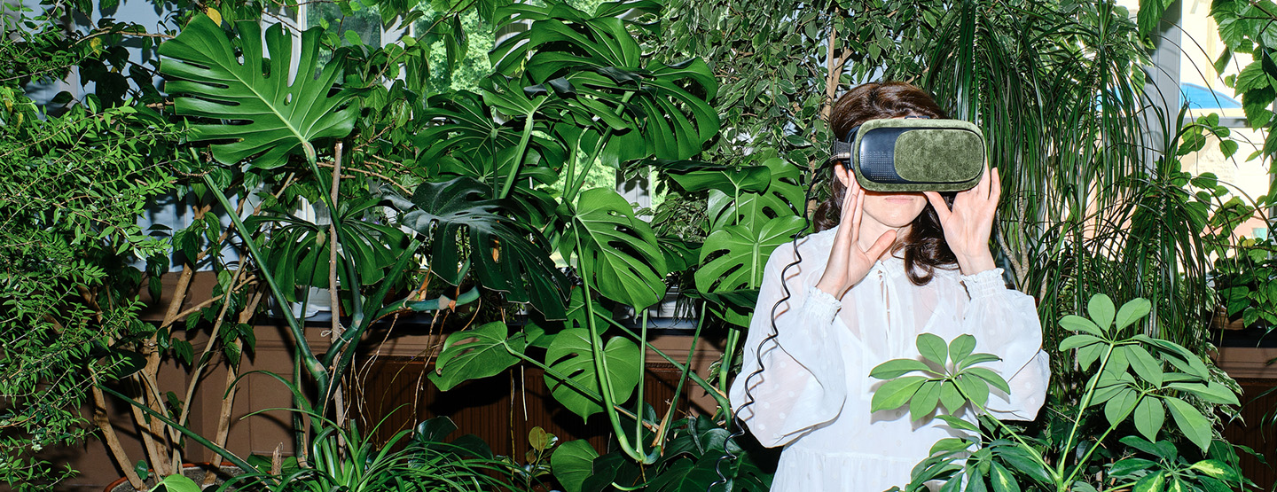 Frau, umringt von Grünpflanzen, blickt durch VR-Brille