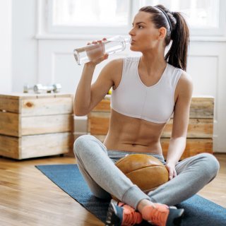 Frau mit Sixpack trinkt Wasser auf Yoga-Matte