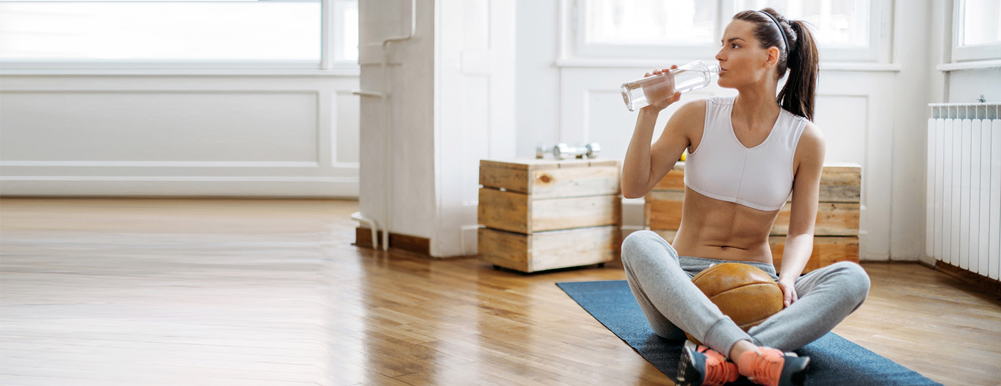 Frau mit Sixpack trinkt Wasser auf Yoga-Matte