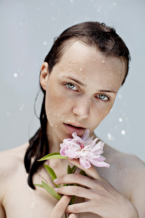 Junge Frau unter einem Wasserschauer mit Blume in den Händen