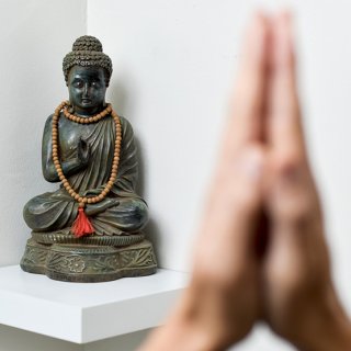 Jemand faltet die Hände vor einer kleinen Buddhafigur