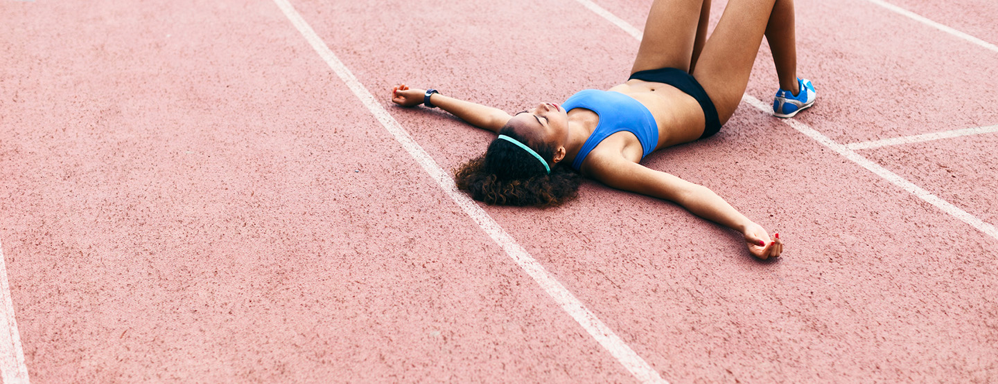 Sportliche Frau liegt erschöpft auf Laufbahn und hat vielleicht schon Muskelkater