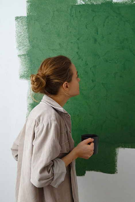 Frau steht mit Teetasse vor algengrün gestrichener Wand